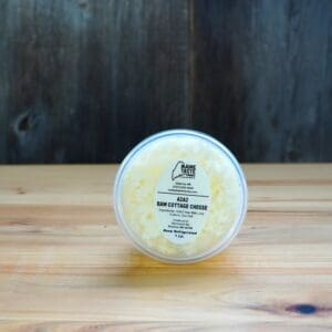 A container of cheese on top of a wooden table.