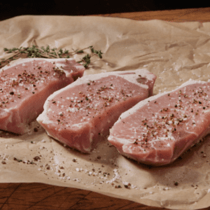 Three raw pork chops on a piece of paper.