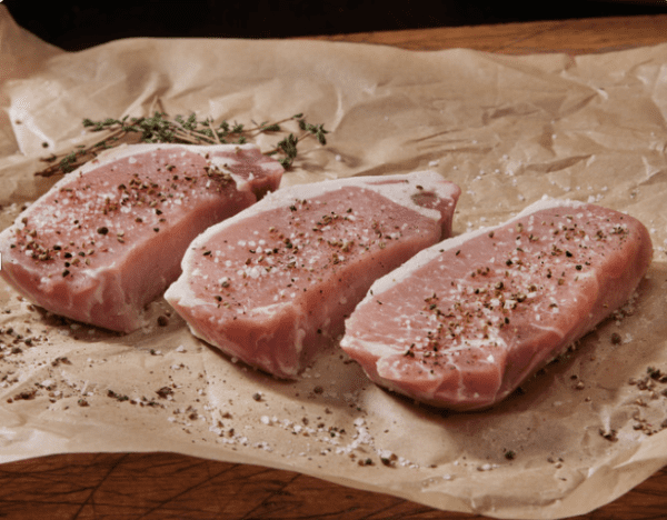 Three raw pork chops on a piece of paper.