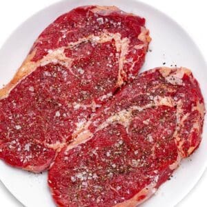 A plate of steak with seasoning on top.