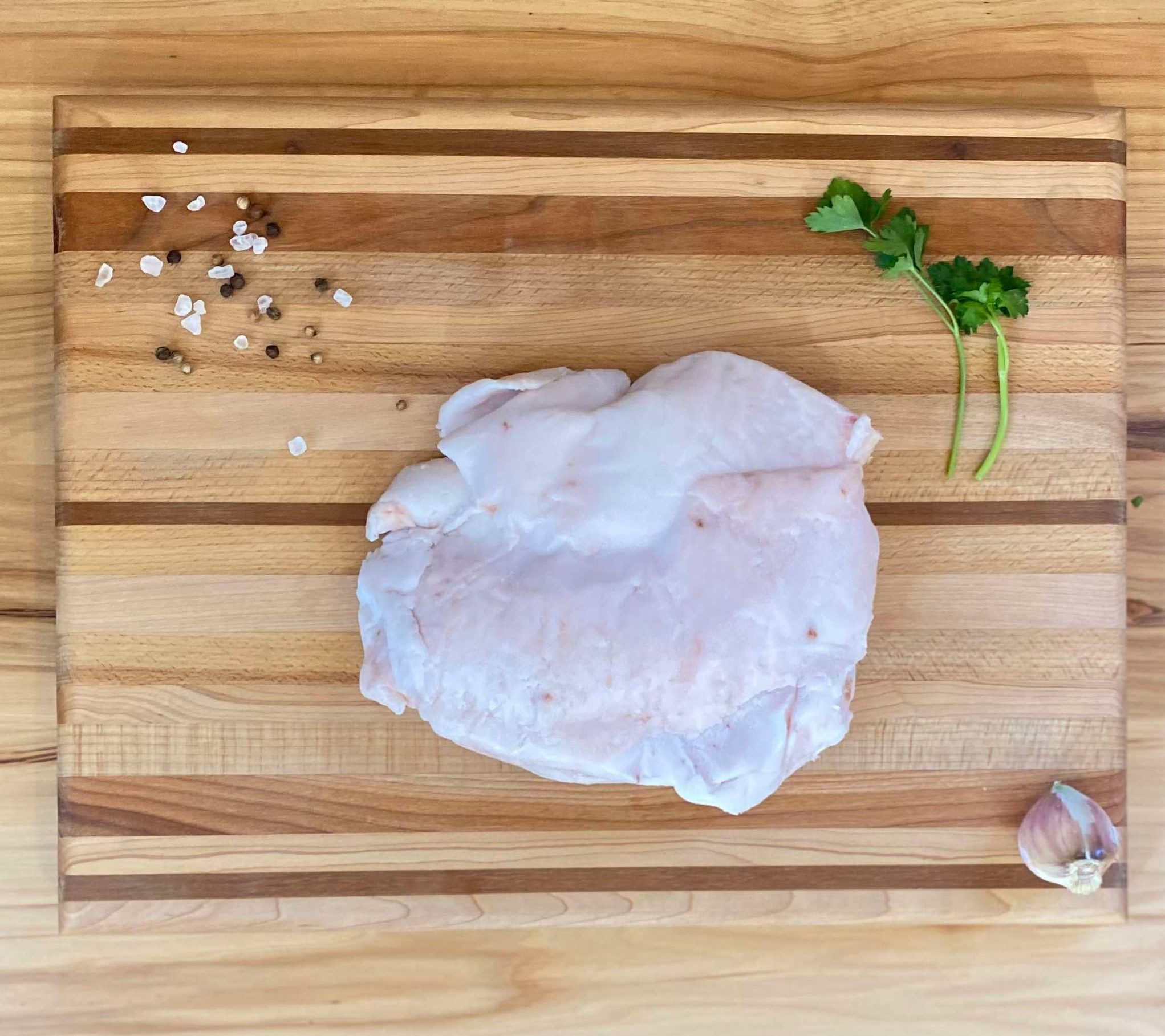A wooden cutting board with meat and garlic on it.