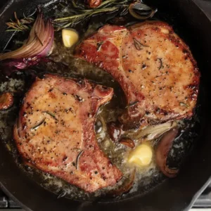 A pan with two pieces of meat in sauce.