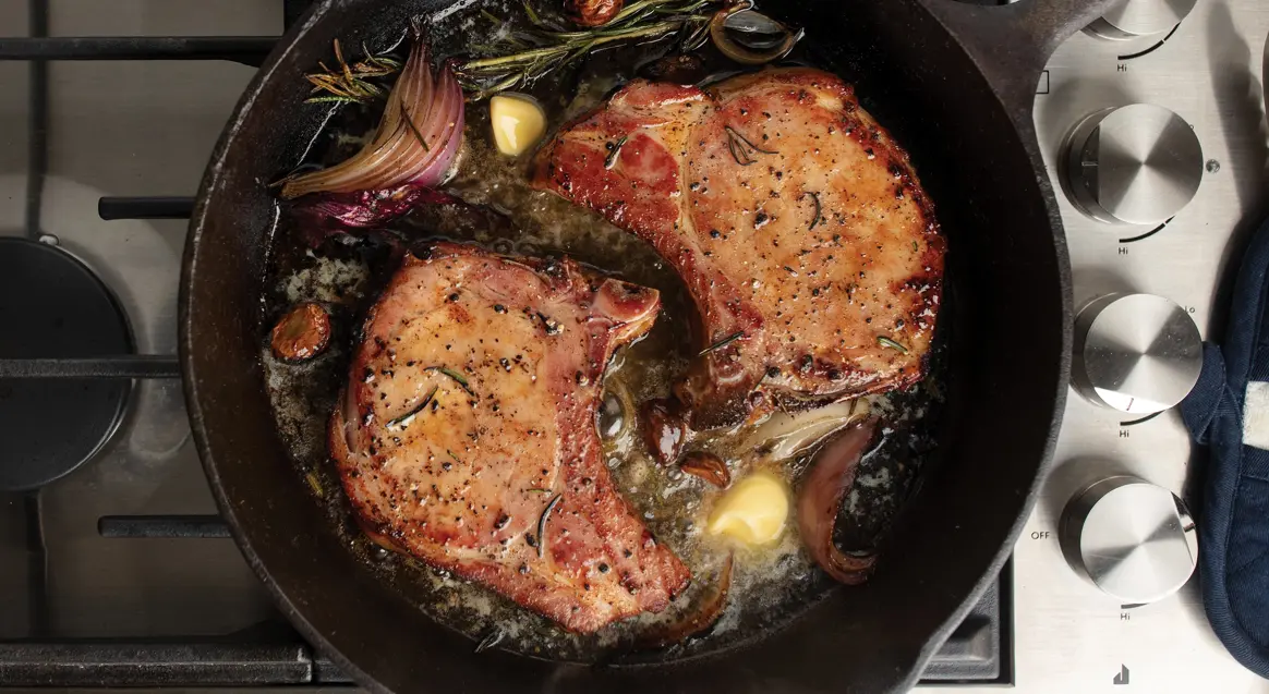 A pan with two pieces of meat in sauce.