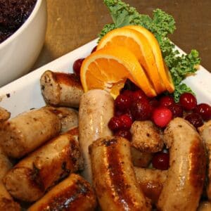 A plate of sausage and fruit on the table.