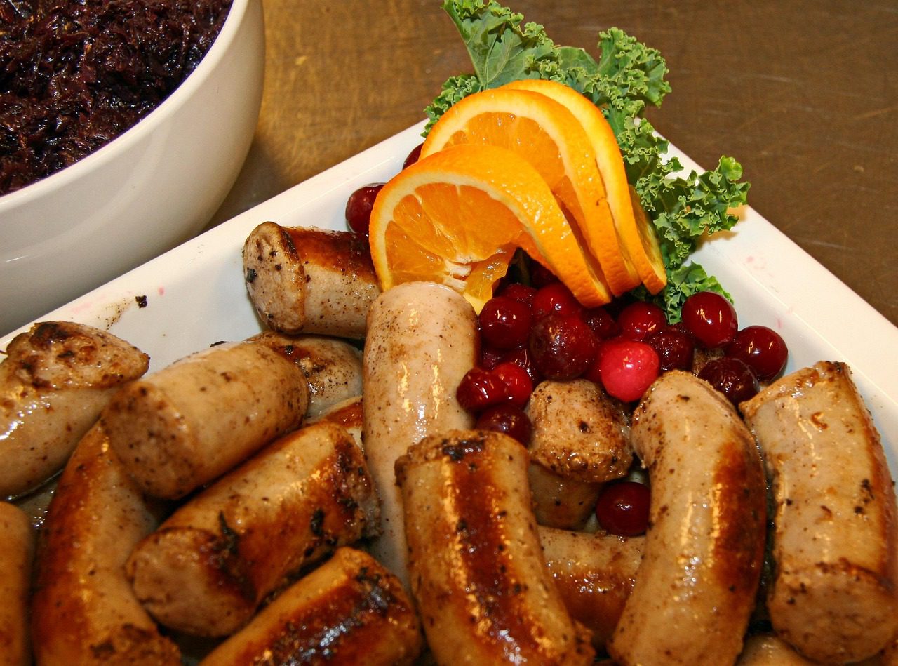 A plate of sausage and fruit on the table.