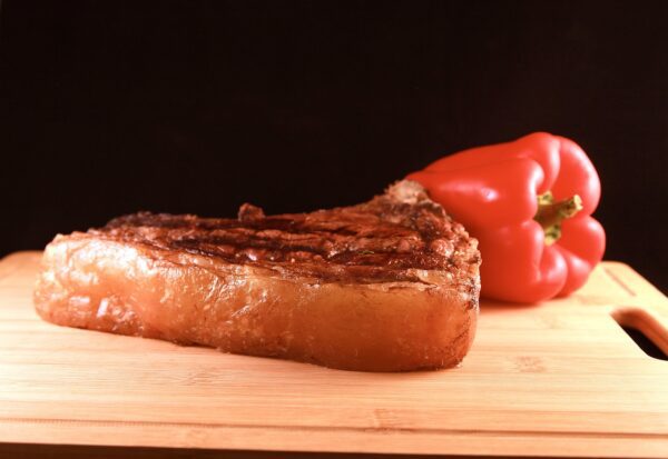 A piece of meat and bell pepper on a cutting board.