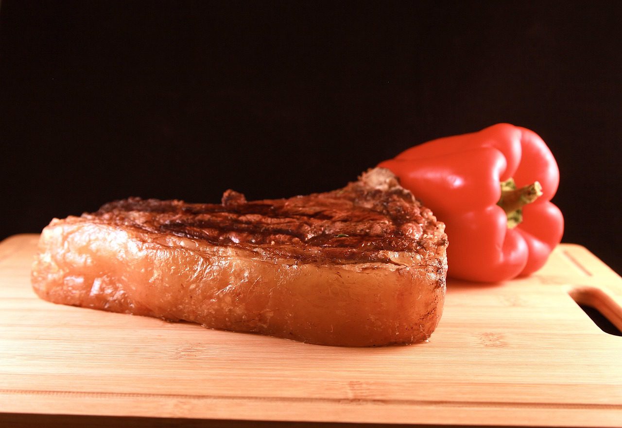 A piece of meat and bell pepper on a cutting board.