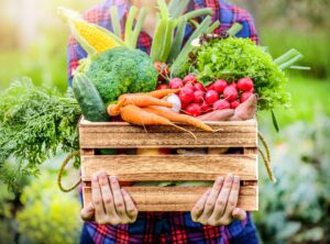 A person holding a crate of vegetables in their hands.