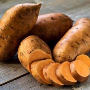 Whole and sliced sweet potatoes on wood table.